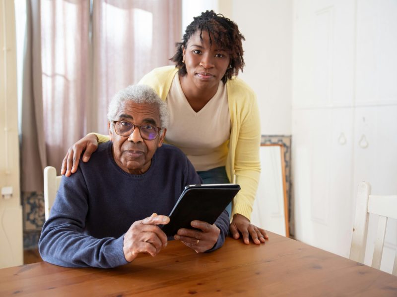 A Woman Standing Beside the Elderly Man Holding a Tablet